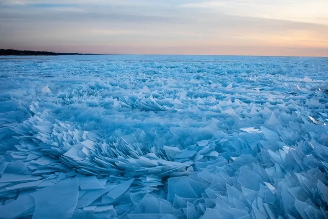 Icy lakefront with frozen waves and winter fog over the skyline